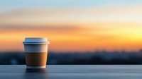 Disposable coffee cup on wooden surface against blurred sunset sky background, creating minimalist composition with warm evening atmosphere.