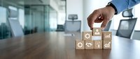 Professional businessman hand arranging wooden blocks with business icons on modern office desk representing strategic planning and corporate growth.