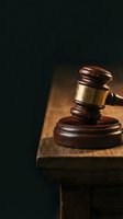Wooden judge gavel with gold band resting on sound block atop a wooden surface against dark background, symbolizing law and justice.