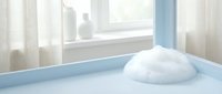 White foam soap bubble on clean blue bathtub edge near window with soft natural light creating peaceful bathroom hygiene and cleanliness concept.