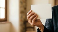 Senior male professional holding blank white card in office environment for corporate messaging and branding purposes.