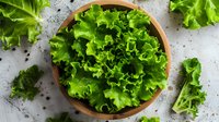 Fresh green lettuce leaves in wooden bowl on concrete background, top view composition for healthy eating and salad preparation concepts.
