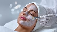 Young woman receiving professional facial mask treatment at spa with cosmetic brush application for skincare and beauty wellness relaxation.
