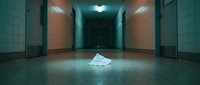 Dimly lit institutional corridor with a crumpled paper on the floor, evoking mystery, abandonment, and suspense in an empty hallway.