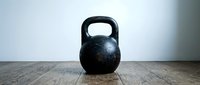 Black kettlebell weight on wooden floor in gym studio. Fitness equipment for strength training, crossfit workouts, and home exercise routines.