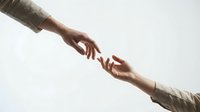 Two hands reaching toward each other in helping gesture against neutral background symbolizing support, connection and teamwork in business.