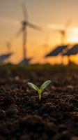 Green seedling sprouting from dark soil with blurred wind turbines and solar panels at sunset, symbolizing renewable energy growth and sustainability.