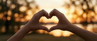 Hands forming a heart shape against a warm golden sunset over a lake, symbolizing love, romance, and connection in nature.