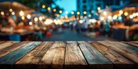 Empty wooden table surface with blurred night market background featuring warm string lights and food stalls for product display and montage.