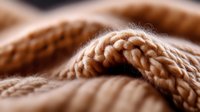 Extreme close-up macro photography of beige knitted wool texture showing detailed yarn pattern and soft fiber structure in warm natural lighting.