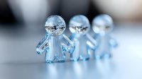 Crystal glass figurines in shape of small people standing in row on reflective surface with soft blurred background creating dreamy atmosphere.