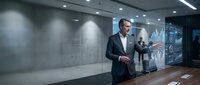 Middle-aged Caucasian businessman in dark suit analyzing financial data on futuristic holographic display in modern office boardroom.