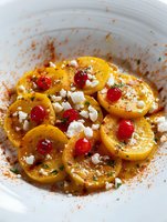 Yellow squash carpaccio garnished with fresh cherries, crumbled feta cheese, herbs and spices on white plate. Vibrant seasonal appetizer with contrasting colors.