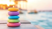 Colorful stacked zen stones with burning candle on top against blurred ocean sunset background, creating peaceful spa and meditation atmosphere.