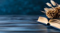 Open book with dried flowers on dark blue background, creating atmospheric composition with soft focus and bokeh effect. Pages flutter in gentle breeze.