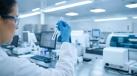 Female scientist in white lab coat examining test tube sample in modern research laboratory with advanced equipment and sterile environment.