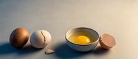 Fresh cracked egg with golden yolk in white bowl and broken eggshells on neutral background for cooking and baking recipes.