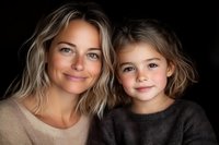 Heartwarming portrait of mother and daughter with gentle smiles against dark background showcasing natural beauty and genuine emotional connection in studio lighting.