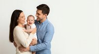 Happy young Caucasian family with baby laughing together against white background. Parents holding infant child in loving embrace for family portraits.