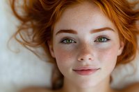 Close up portrait of young woman with natural red hair, green eyes and freckles lying down, looking at camera with gentle smile. Natural beauty concept.