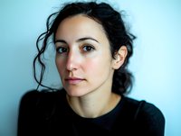 Young brunette woman with curly hair in black top against blue background. Natural portrait for lifestyle and wellness content.