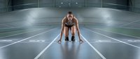 Athletic woman in starting position on indoor track ready to sprint in modern sports facility with professional lighting for fitness and training concepts.