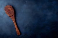Rustic wooden cooking spoon on dark blue textured background with dramatic lighting and copy space for menu, recipe or culinary design.