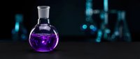 Purple liquid in round glass flask on dark laboratory table with blurred scientific equipment background for chemistry research and pharmaceutical development.