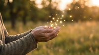 Mature adult hands cupped together releasing glowing magical particles in sunlit outdoor field setting, symbolizing hope, wishes, spirituality, and positive energy transformation.