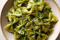 Fresh farfalle pasta with vibrant green pesto sauce and herbs served in ceramic bowl, ready for Italian cuisine menu or cooking blog content.