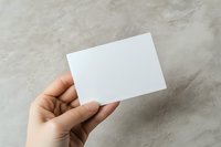 Cropped hand holding blank white card against concrete background, ready for branding, business card mockup, or corporate identity design.