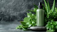 Green cosmetic bottle with pump dispenser surrounded by fresh aloe vera plants and herbs on stone surface for natural skincare and beauty products.