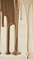 Liquid chocolate or caramel dripping onto textured beige fabric surface, creating flowing streams and pooling effects for food, beverage, and culinary design projects.