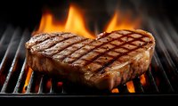 Heart shaped grilled beef steak with grill marks and flames on barbecue grate, juicy meat cooking on hot charcoal grill, romantic dinner concept.