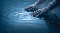 Two hands touching water surface creating ripples in deep blue liquid, suitable for wellness, spa, and environmental concepts.