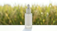 Clear glass dropper bottle with white pipette on clean surface against blurred green foliage background for skincare and cosmetic product mockups.