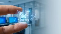 Close-up of hand holding glowing trend icon with upward arrow graph in modern office environment for business analytics and growth strategy.