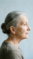Senior woman with gray hair in profile view wearing casual beige sweater against neutral background. Suitable for healthcare, wellness, aging, and lifestyle editorial use.