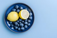Fresh lemon and ripe blueberries on a blue ceramic plate, top view, pastel background, healthy eating concept for food blogs and recipes.