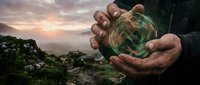 Hands holding glowing green earth globe over mountain landscape at sunset, symbolizing environmental protection and sustainability awareness.