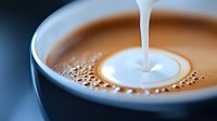 Pouring cream creates heart shape in coffee cup, close-up view showing rich brown coffee with white milk stream and delicate foam bubbles on surface.
