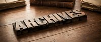 Vintage wooden letterpress blocks spelling ARCHIVES on rustic wooden surface with old books, evoking history, records, and document storage.