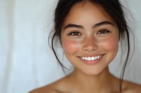 Young Asian woman with natural freckles and radiant smile against white background, displaying genuine happiness and confidence in casual portrait setting.