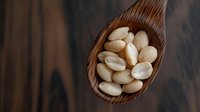 Whole blanched almonds in wooden spoon on dark background, macro food photography showing texture and natural ingredients for healthy eating and cooking.