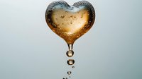 Heart-shaped water drop with golden light and tiny bubbles falling against soft gray background, creating romantic and dreamy atmosphere for valentines designs.