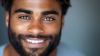 Young African American man with bright genuine smile and beard against blurred background, displaying confidence and joy in professional headshot style portrait.
