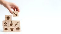 Hand placing wooden cube with watering can icon completing gardening symbol puzzle on white background for agricultural business concepts.