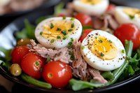 Fresh tuna salad with halved boiled eggs, cherry tomatoes, green beans and chives on black plate, close up view with selective focus. Perfect for menu.