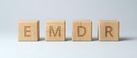 Wooden blocks spelling EMDR letters arranged in row on white background for therapy and mental health treatment concepts.