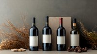 Wine bottles with blank labels arranged against dark background with dried flowers and natural decorative elements creating rustic wine tasting atmosphere.